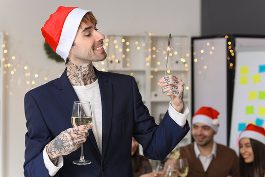 Young man with champagne and sparkler celebrating New Year at corporate party in office
