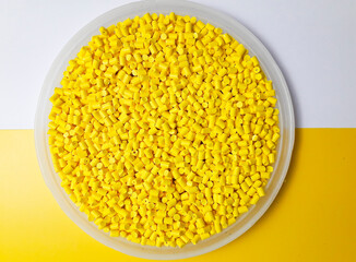 Yellow masterbatch granules in a cup on a yellow and white background, a color pigment carrier polymer in the plastics industry.