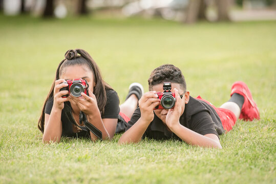 Boy and girl laying in the grass taking photos with their cameras