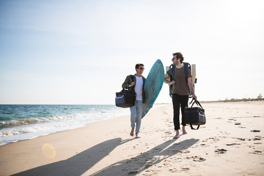 Two men with cooler bag and surfboard at the beach on a sunny day