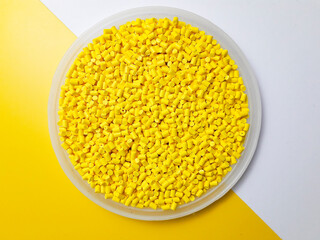 Yellow masterbatch granules in a cup on a yellow and white background, a color pigment carrier...