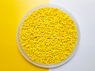 Yellow masterbatch granules in a cup on a yellow and white background, a color pigment carrier...