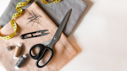 Sewing tools and fabrics. Scissors, thread, measuring tape, needles, and pins on soft cloth