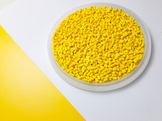 Yellow masterbatch granules in a cup on a yellow and white background, a color pigment carrier...