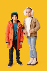 Cute little happy children in warm winter clothes on yellow background