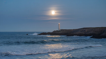 solitary lighthouse stands majestically by ocean under full moon, casting serene glow on waves. tranquil scene evokes sense of peace and solitude