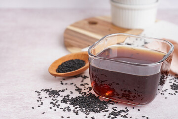 Bowl of oil with wooden spoon and sesame seeds on white background