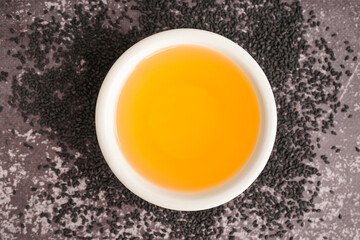 Bowl of oil with sesame seeds on grey grunge background