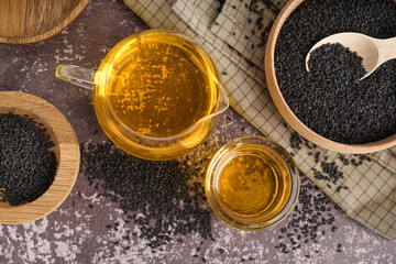 Jug and glass of oil with sesame seeds on grey grunge background