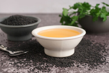 Bowl of oil with spoon and sesame seeds on grey grunge background