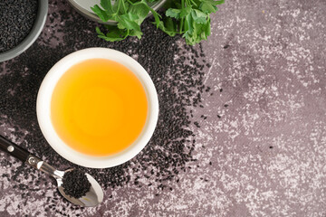 Bowl of oil with spoon, parsley and sesame seeds on grey grunge background