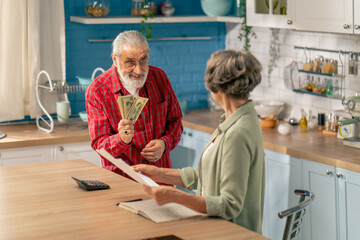 Fototapeta premium in bright kitchen an elderly cute couple at the table count their expenses monthly payment summing up the results of the year utilities count monthly survival count money