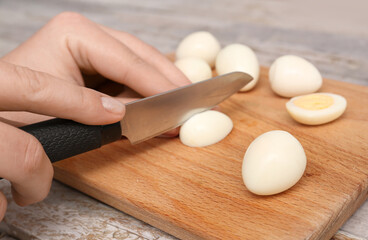 Woman cutting fresh boiled quail eggs on wooden table, closeup