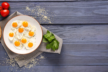 Plate with fried quail eggs, parsley and tomatoes on blue wooden background