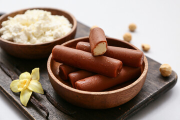 Wooden board with tasty chocolate glazed curd snacks with vanilla flavor on light background, closeup