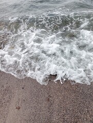 Portrait of waves, sand and small rocks on the beach
