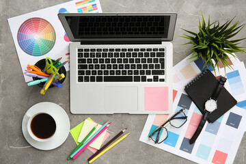 Workplace of graphic designer with laptop, pencils and color charts on grey grunge table