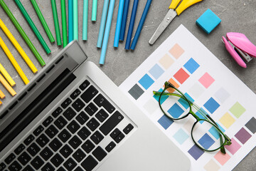Workplace of graphic designer with laptop, pencils and color charts on grey grunge table