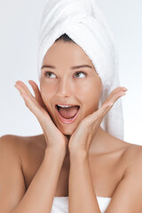 A young Caucasian woman with a towel wrapped around her head expresses excitement and joy, her hands framing her face in a playful gesture. This high-energy image is ideal for beauty, skincare, and