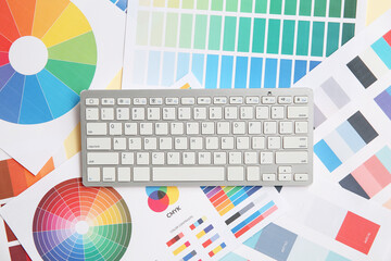 Workplace of graphic designer with keyboard on color charts
