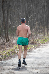 A man is running in the woods with no shirt on