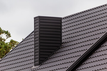 Facing the chimney with metal tiles. Black color of the roof. New roof design