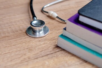 A stethoscope on a wooden table with a stack of textbooks. Copy space for text. Medical study,...