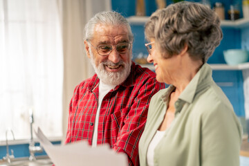 close up in bright kitchen an elderly cute couple at the table count their expenses monthly payment summing up the results of the year utilities count monthly survival count money laughing