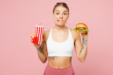 Young sad woman wears white casual clothes hold eat burger, bottle of soda pop water, french fries...