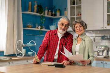 Fototapeta premium in bright kitchen an elderly cute couple at the table count their expenses monthly payment summing up the results of the year utilities count monthly survival count money laughing