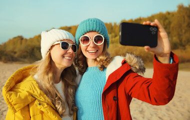 Happy young two women friends taking selfie with phone on beach, smiling girlfriends having fun