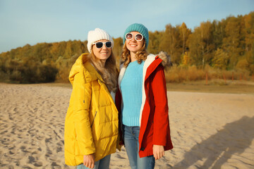 Happy young two women friends on sunny beach, stylish girlfriends smiles together on sea coast