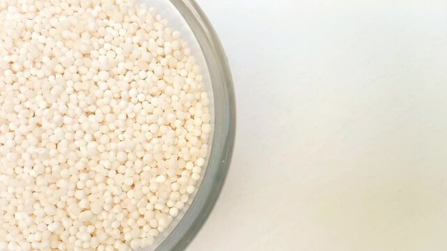 Half of circle shaped Sago pearls or tapioca pearls glass bowl in the left half of the frame, rotating, isolated on the white background, closeup, herbs and spices
