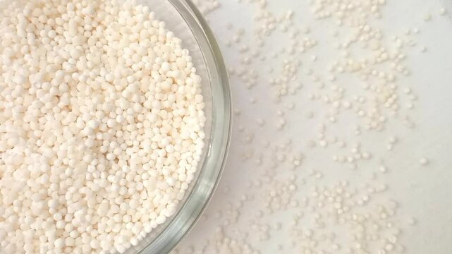 Half of circle shaped Sago pearls or tapioca pearls glass bowl spices spilled around it, left half of the frame, rotating, white background, closeup, herbs and spices
