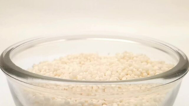 Sago pearls or tapioca pearls drops in a glass bowl on white background, a glass bowl full of sago pearls or tapioca pearls in the center, rotating, micro shot, herbs and spices
