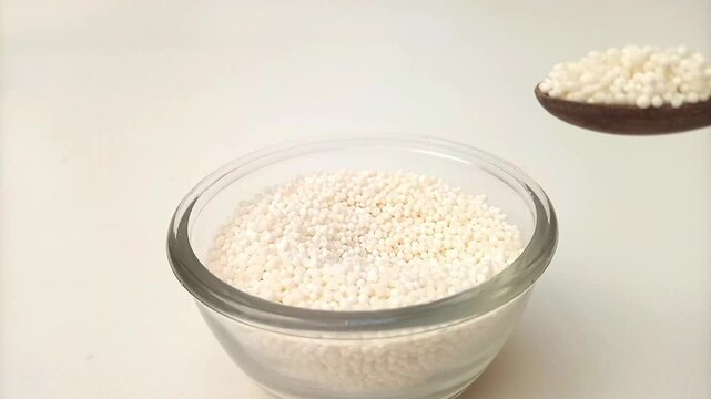 Spoon out of Sago pearls or tapioca pearls from the glass bowl with a wooden spoon, herbs and spices