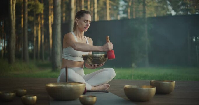 Portrait of a Woman Gently Making a Resonant Sound From the Singing Bowl by Gliding the Stick Along Its Rim. Meditative Tone Deepens Her Practice, Filling the Space With Calming Vibrations