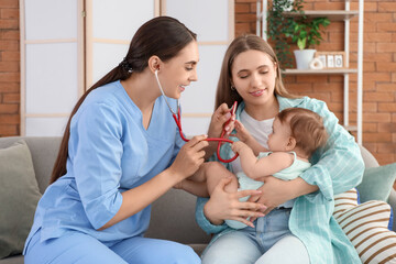 Female pediatrician with stethoscope listening to little baby and mother on sofa at home