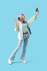 Female student with photo camera taking selfie on blue background