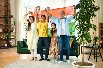 Fototapeta premium Indian family celebrating victory on TV, waving the tricolor flag joyfully from their sofa