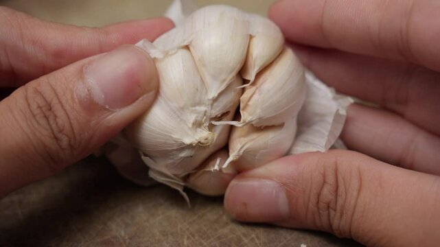 Hands peeling cloves of garlic over a kitchen counter, preparing ingredients for cooking in a cozy kitchen setup