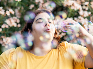 A woman with neurodiversity blows bubbles as colorful spheres float around her. She is surrounded...