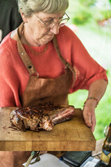 Senior woman preparing grilled meat at outdoor barbecue