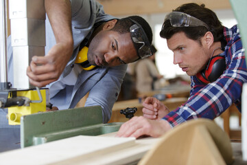 carpenter showing apprentice how to use sawing machine