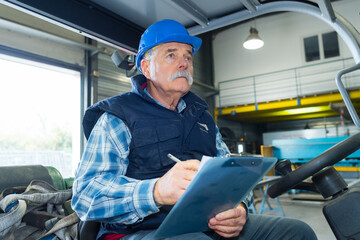 senior forklift driver making notes on clipboard