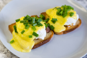 Delicious English breakfast. Eggs benedict with sauce and bacon on toasted white bread on a gray plate, close-up on a light background