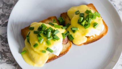 Delicious English breakfast. Eggs benedict with sauce and bacon on toasted white bread on a gray plate, close-up on a light background