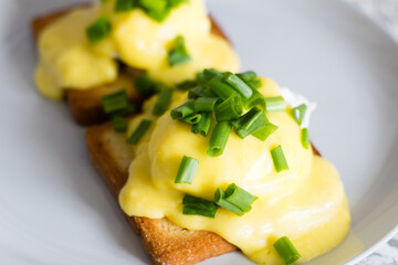 Delicious English breakfast. Eggs benedict with sauce and bacon on toasted white bread on a gray plate, close-up on a light background