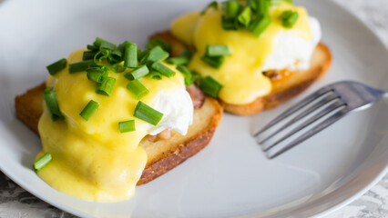 Delicious English breakfast. Eggs benedict with sauce and bacon on toasted white bread on a gray plate, close-up on a light background