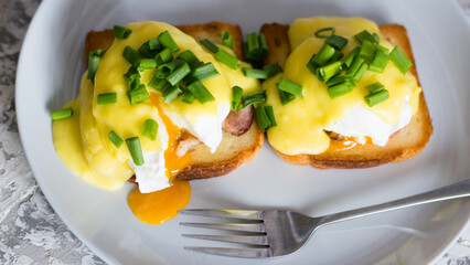 Delicious English breakfast. Eggs benedict with sauce and bacon on toasted white bread on a gray...
